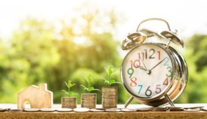 A clock sits next to three stacks of coins and a small house, representative of property management SEO as explained in this blog A clock sits next to three stacks of coins and a small house, representative of property management SEO as explained in this blog